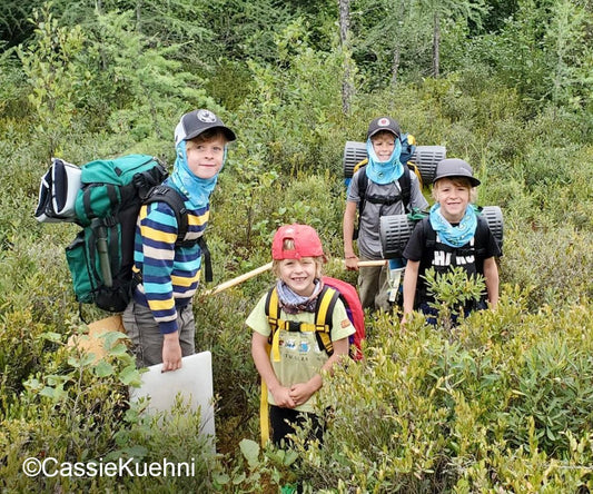 canoe trip with kids carrying canoe packs on portage in tall grass